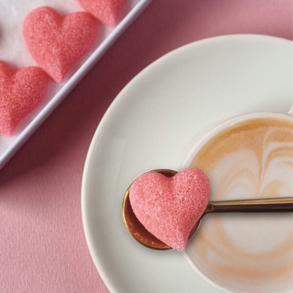 Sucre en forme de cœur, de couleur rose, poser sur une cuillère au-dessus d'une tasse à café