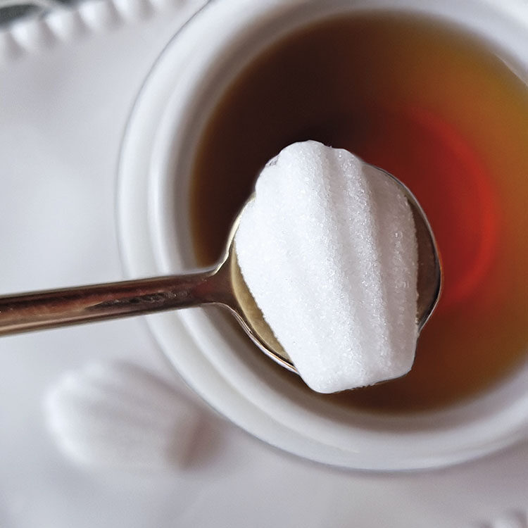Sucre blanc, en forme de madeleine posé sur une cuillère au-dessu d'une tasse de thé