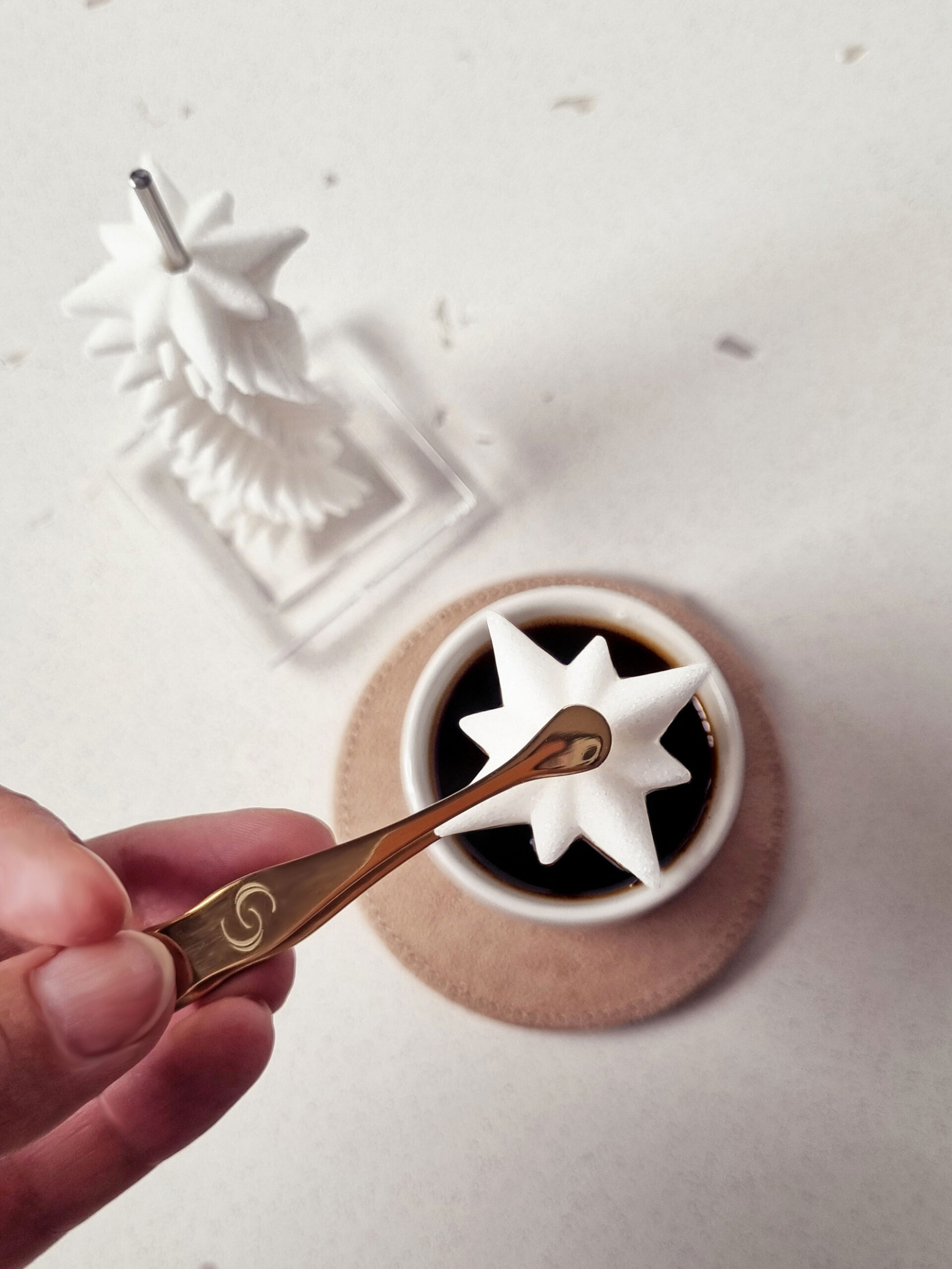main tenant une pince à sucre, qui dépose un sucre en forme d'étoile dans une tasse de café